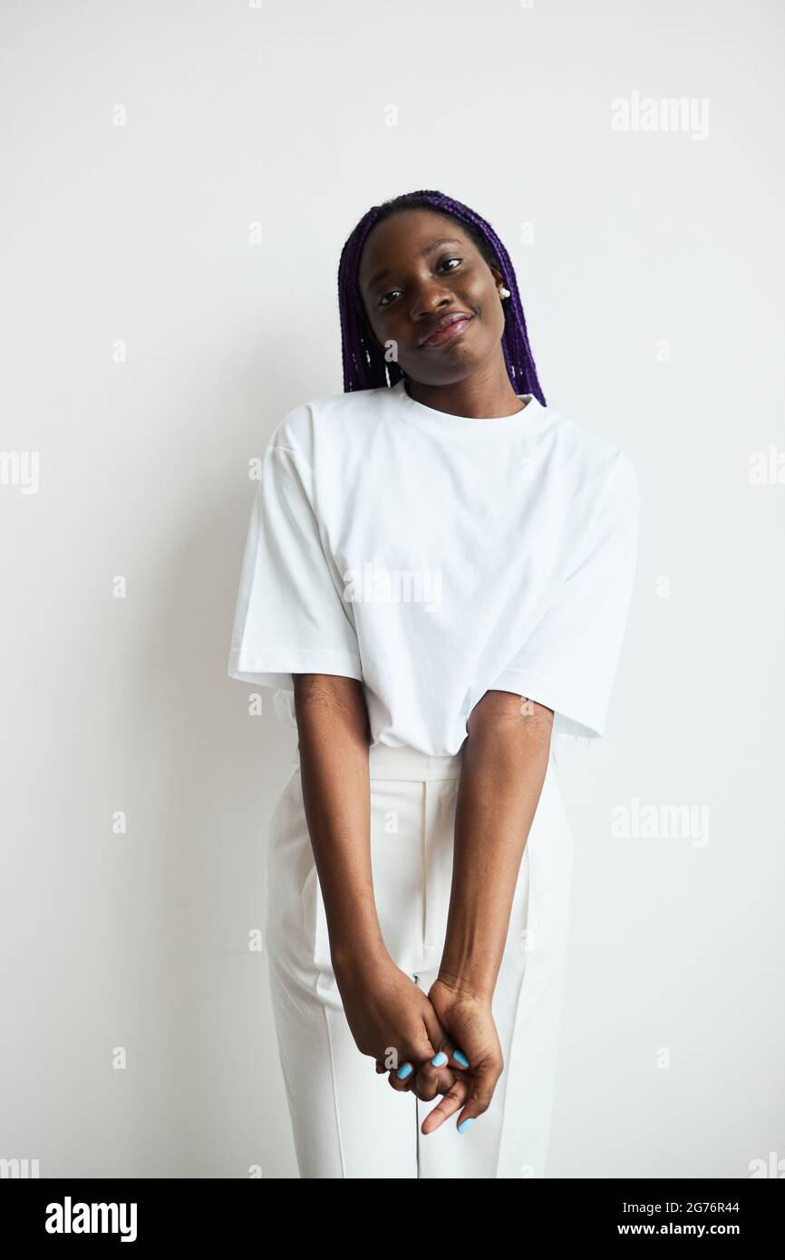 Ritratto verticale minimo di giovane afroamericana con capelli colorati che sorridono alla fotocamera mentre si sta in piedi su sfondo bianco Foto Stock