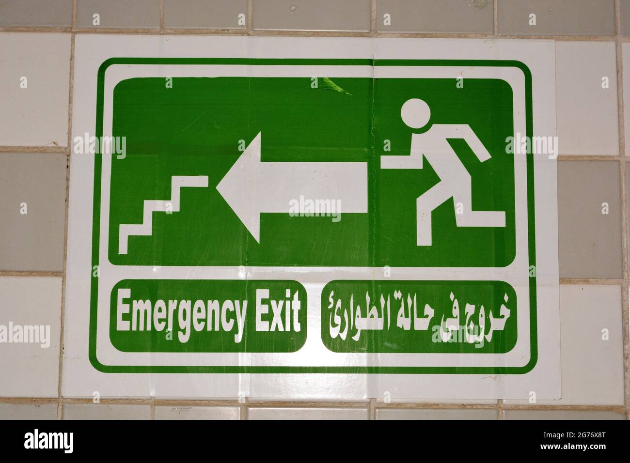 Segnale di uscita di emergenza antincendio nel corridoio indica la via di uscita dall'edificio per fuggire in caso di emergenza, urgenza e incendio, tradotto parole arabe ( uscita in Foto Stock