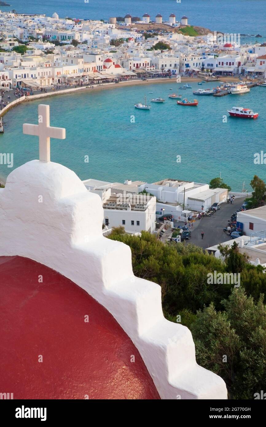 Chiesa a cupola rossa con croce bianca che domina la città di Mykonos e il porto sulla costa del mar Egeo nelle isole greche Foto Stock