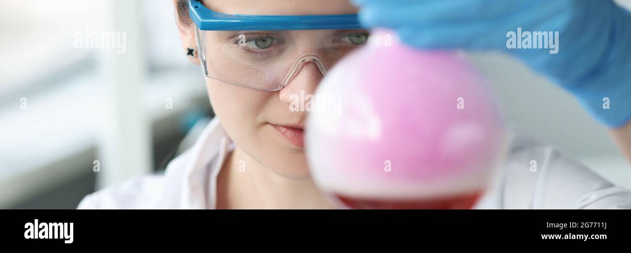 Donna ricercatrice in occhiali sta conducendo esperimenti chimici in fiasca Foto Stock