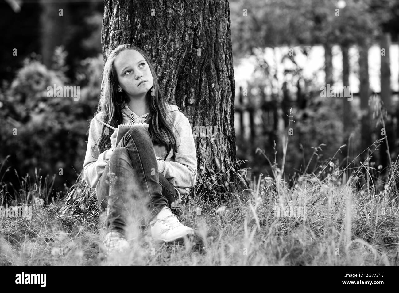 Teengirl scrivere in un notebook seduto nel parco. Foto in bianco e nero. Foto Stock