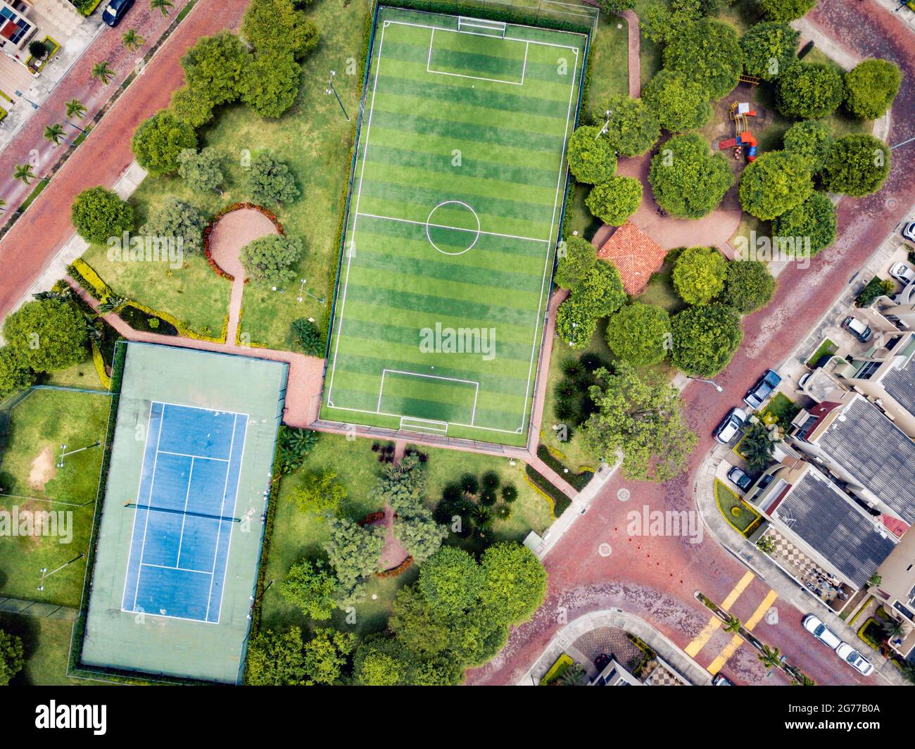 Tiro drone diretto di campo da calcetto vuoto e campo tenis circondato da parco e alberi in una comunità recintata fuori Guayaquil City, Ecuador. Foto Stock