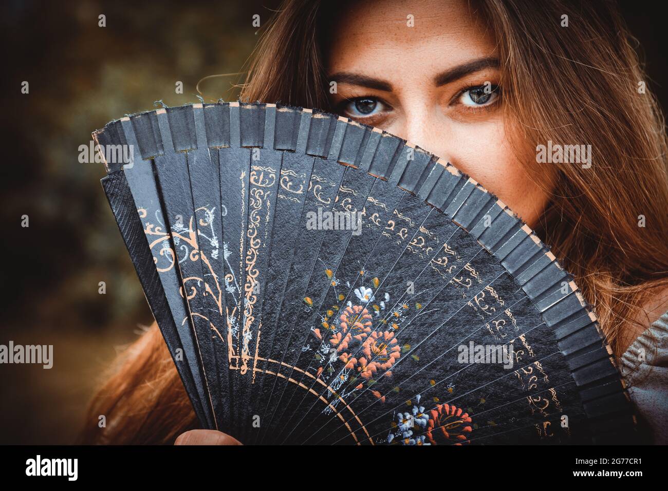 Giovane femmina caucasica che si pone dietro un ventilatore nero Foto Stock