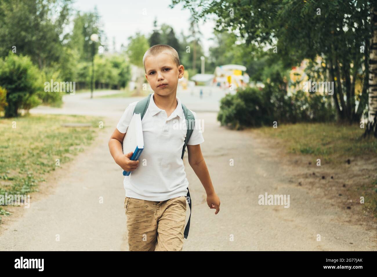 Il ragazzo serio, studente di scuola elementare, a piedi a scuola con borsa dietro e libro. Gli studenti sono pronti per il nuovo anno. Ritorno a scuola. Foto Stock
