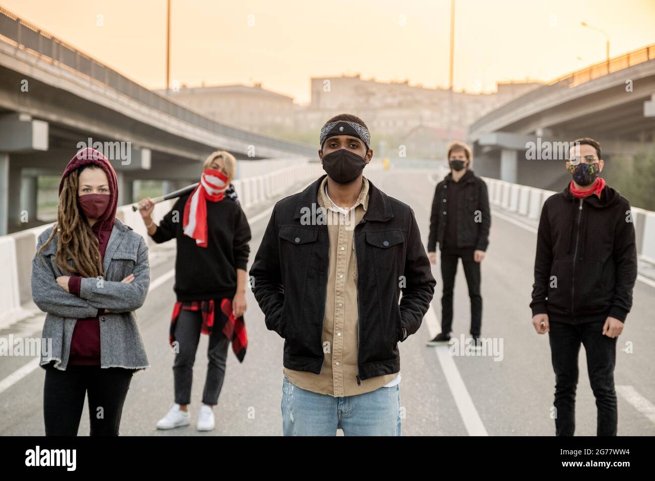 Gruppo di giovani interrazziali in maschere in piedi su strade vuote in città e rivendicare i loro diritti all'alba Foto Stock
