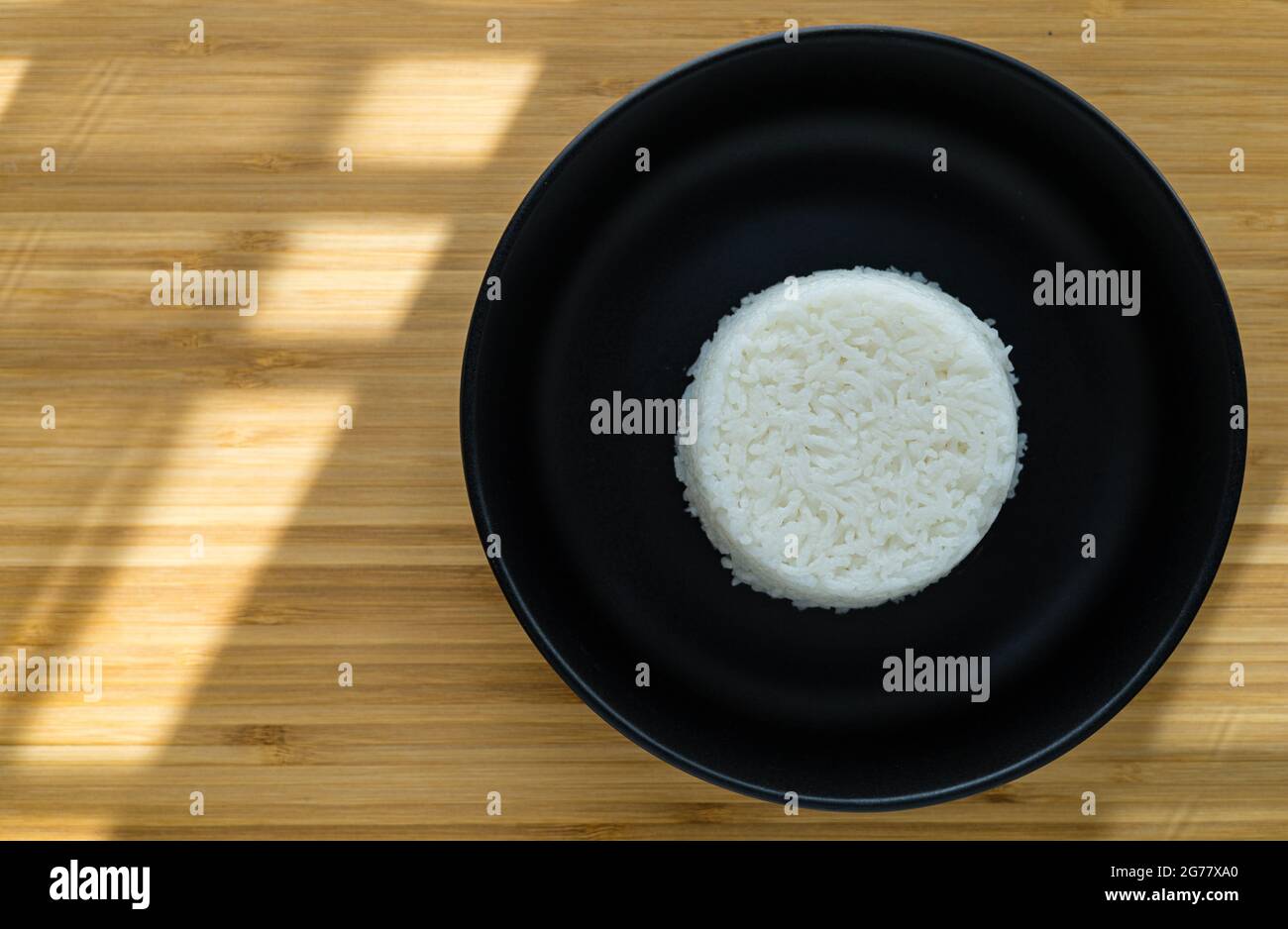 Riso di cottura a vapore di stile thailandese messo su piatto nero su sfondo di legno con spazio di copia. Angolo di visualizzazione superiore Foto Stock