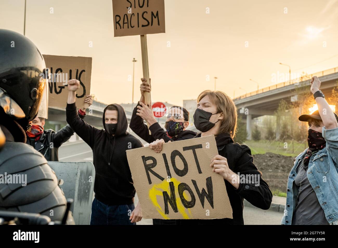 Gruppo di persone scontenti in maschere con segni che rivendicano pari diritti per tutte le etnie, mentre gridano contro la polizia antisommossa su strada Foto Stock