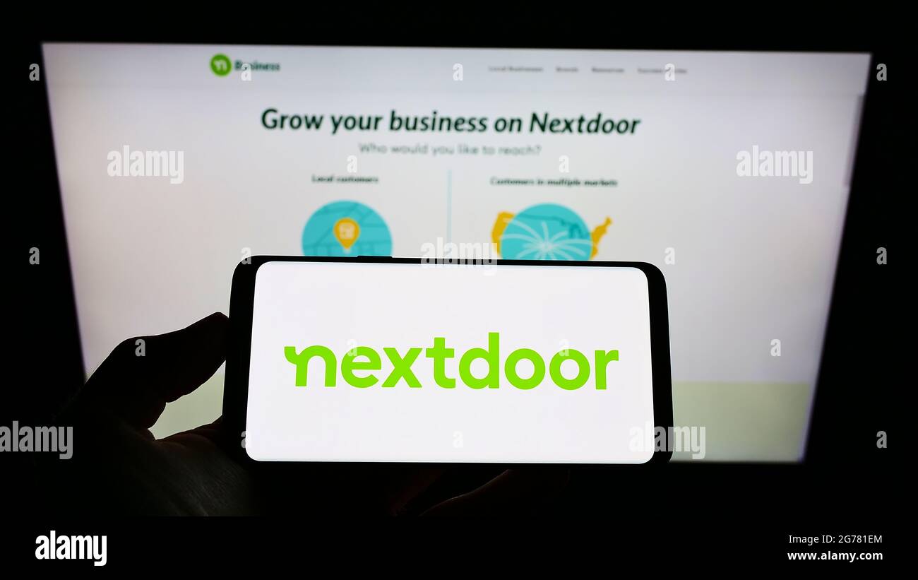 Persona che detiene il telefono cellulare con il logo della società americana di social network Nextdoor Inc. Sullo schermo davanti alla pagina web. Mettere a fuoco il display del telefono. Foto Stock