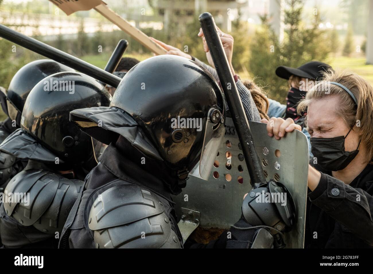 Gruppo di poliziotti in caschi utilizzando maniglie a forma di sIDE mentre si fermano i manifestanti con scudi sulla strada Foto Stock