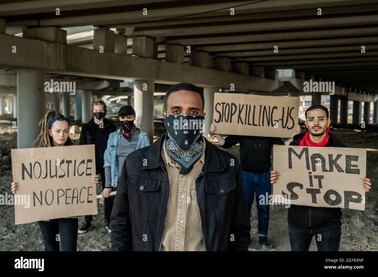 Gruppo di giovani estremisti multietnici in testa a Black man con bandana in piedi con striscioni sotto il ponte Foto Stock