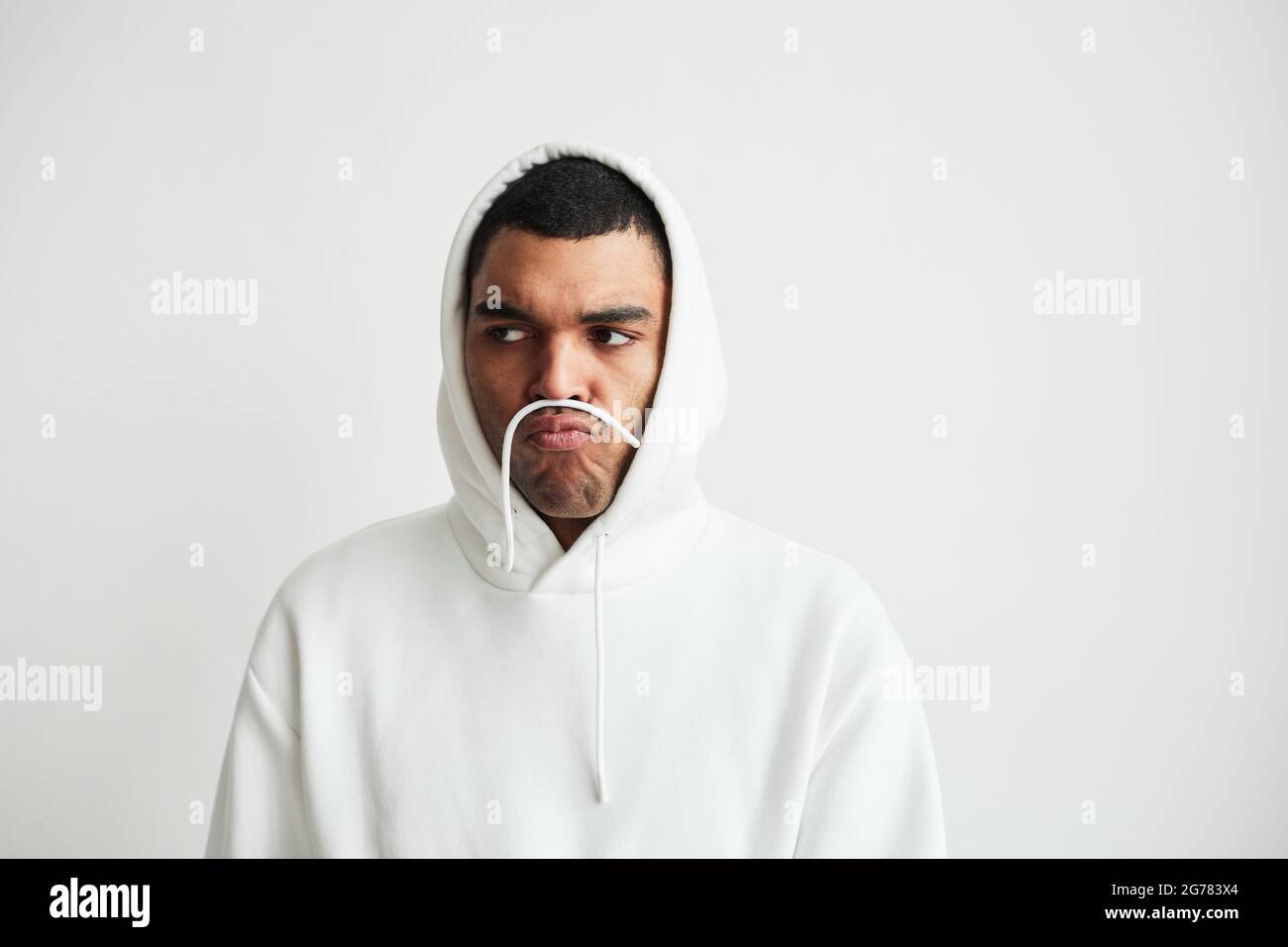 Ritratto minimale di giovane uomo che indossa una felpa con cappuccio e che fa i volti, spazio copia Foto Stock