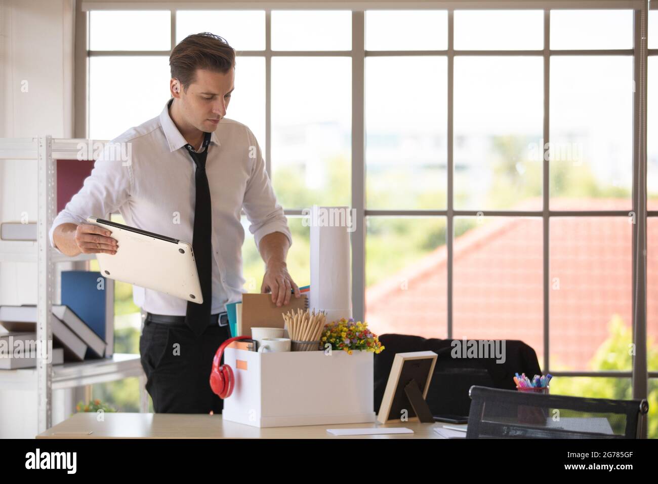 Il giovane uomo d'affari caucasico ha messo il computer portatile e gli effetti personali in scatola di carta prepararsi a tornare a casa alla fine del giorno dopo essere stato licenziato dal suo lavoro. Con Foto Stock