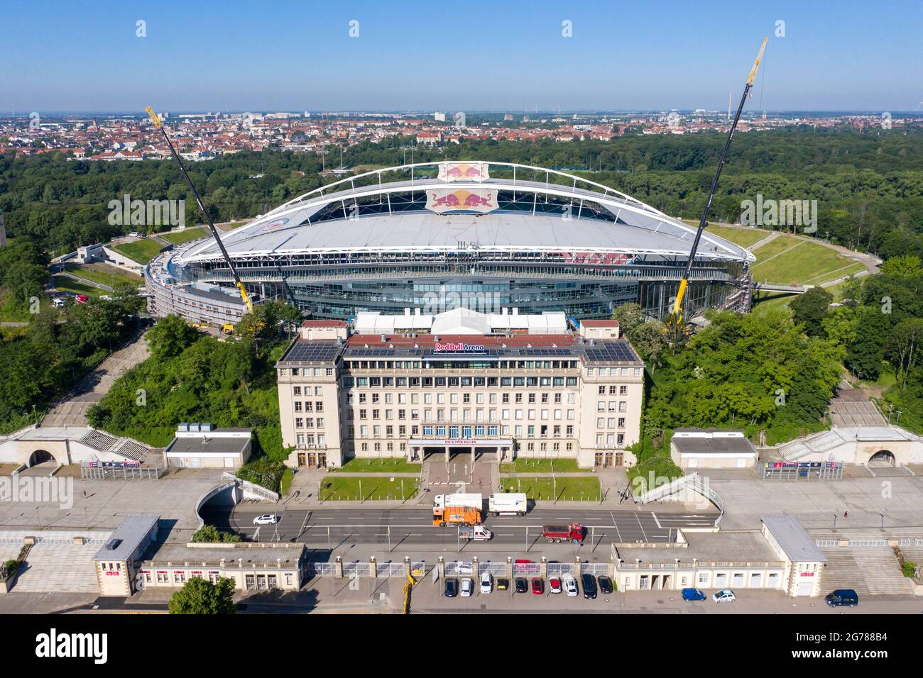 14 giugno 2021, Sassonia, Lipsia: Due gru si trovano alla Red Bull Arena. La casa di RB Leipzig è in fase di ricostruzione. La capacità dello spettatore aumenta da 42,558 a 47,069 in piedi e seduti. L'esterno dello stadio è chiuso con una facciata insonorizzata. L'argine dell'ex Zentralstadion, che comprende l'arena, è stato aperto dietro lo storico campanile per fare spazio ad un nuovo ingresso. RB Leipzig sta investendo nella conversione 60 milioni di euro entro il 2022. (Vista aerea con drone) Foto: Jan Woitas/dpa-Zentralbild/ZB - NOTA IMPORTANTE: In conformità con le norme di t Foto Stock