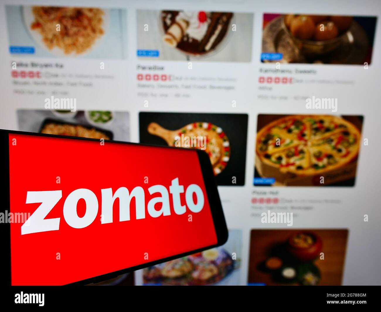 Smartphone con logo della società indiana di ordinazione di alimenti online Zomato sullo schermo di fronte al sito web aziendale. Mettere a fuoco al centro-sinistra del display del telefono. Foto Stock