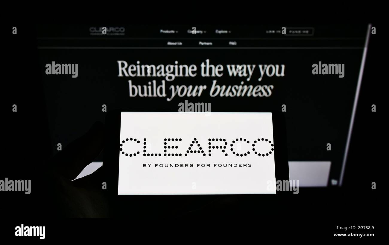 Persona che detiene il telefono cellulare con il logo della società finanziaria americana Clearco sullo schermo di fronte alla pagina web aziendale. Mettere a fuoco il display del telefono. Foto Stock