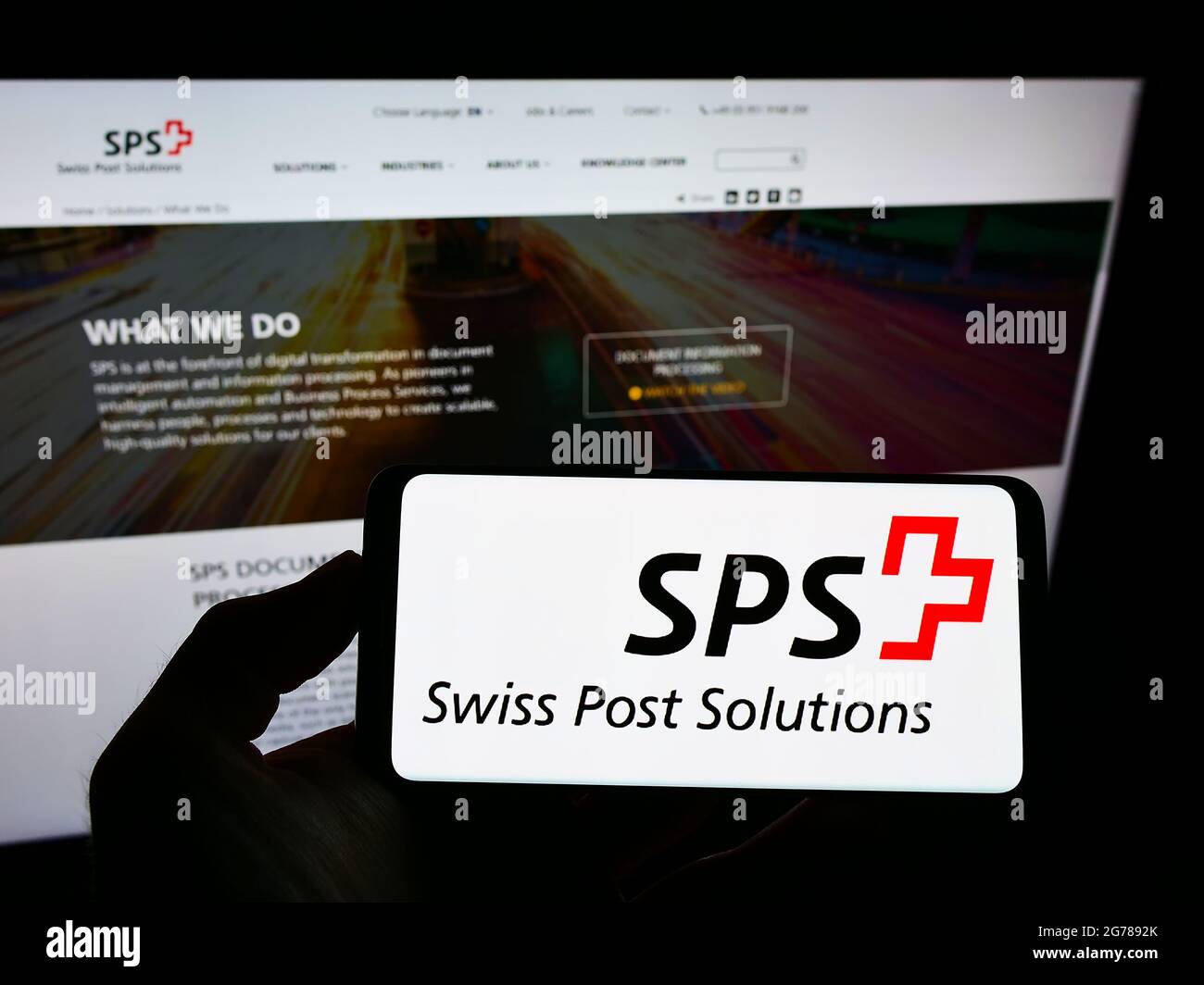 Persona in possesso di smartphone con il logo della società di gestione dei documenti Swiss Post Solutions (SPS) sullo schermo davanti al sito web. Mettere a fuoco il display del telefono. Foto Stock