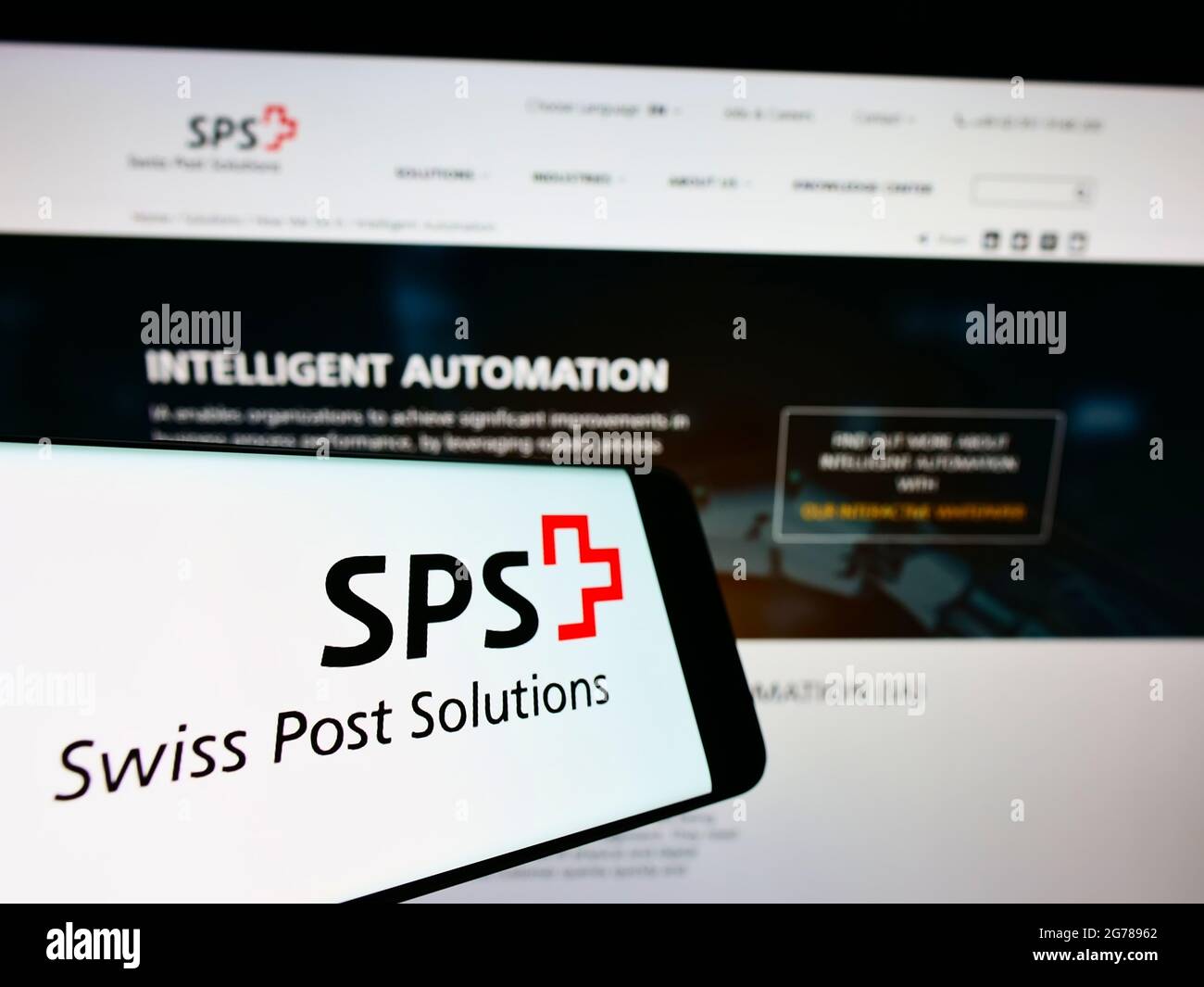 Telefono cellulare con logo dello studio di gestione documenti Swiss Post Solutions (SPS) sullo schermo davanti al sito. Mettere a fuoco il centro-destra del display del telefono. Foto Stock