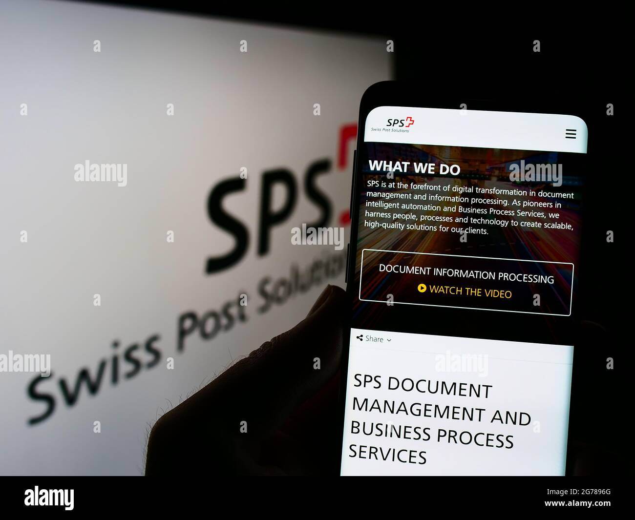 Persona che tiene il telefono con la pagina web dello studio di gestione dei documenti Swiss Post Solutions (SPS) su schermo con il logo. Mettere a fuoco il centro del display del telefono. Foto Stock