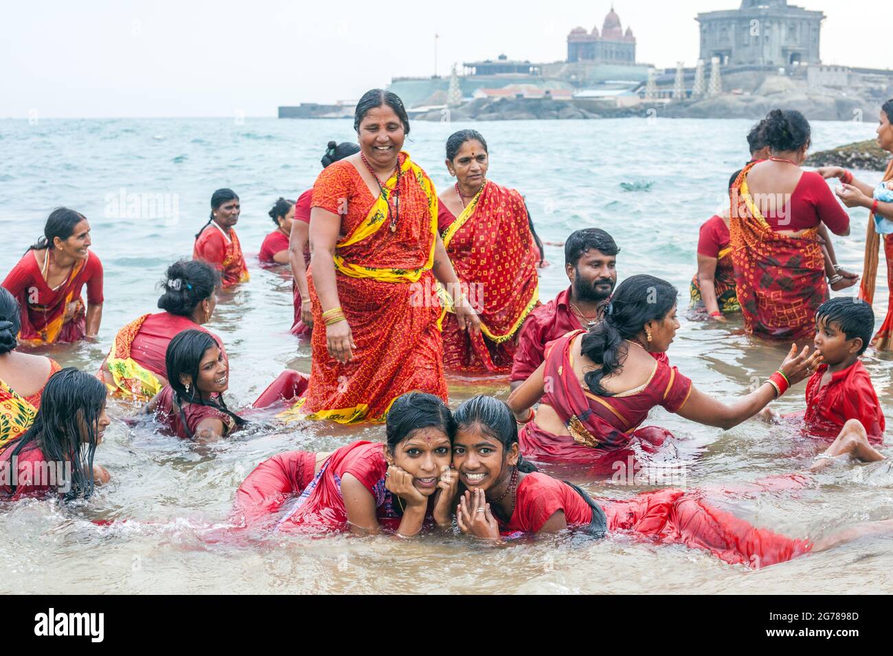 Gruppo di adoratori indù che indossano un bagno di abbigliamento rosso nel Mare di Laccadive di fronte al Vivekananda Rock Memorial, Kanyakumari, , Tamil Nadu, India Foto Stock