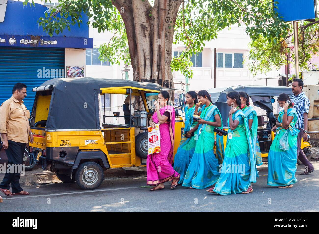 Gruppo di studenti universitari indiani attraenti vestiti con sari blu/verdi dello stesso colore camminare passato auto rickshaws parcheggiato, Kanyakumari, Tamil Nadu, India Foto Stock