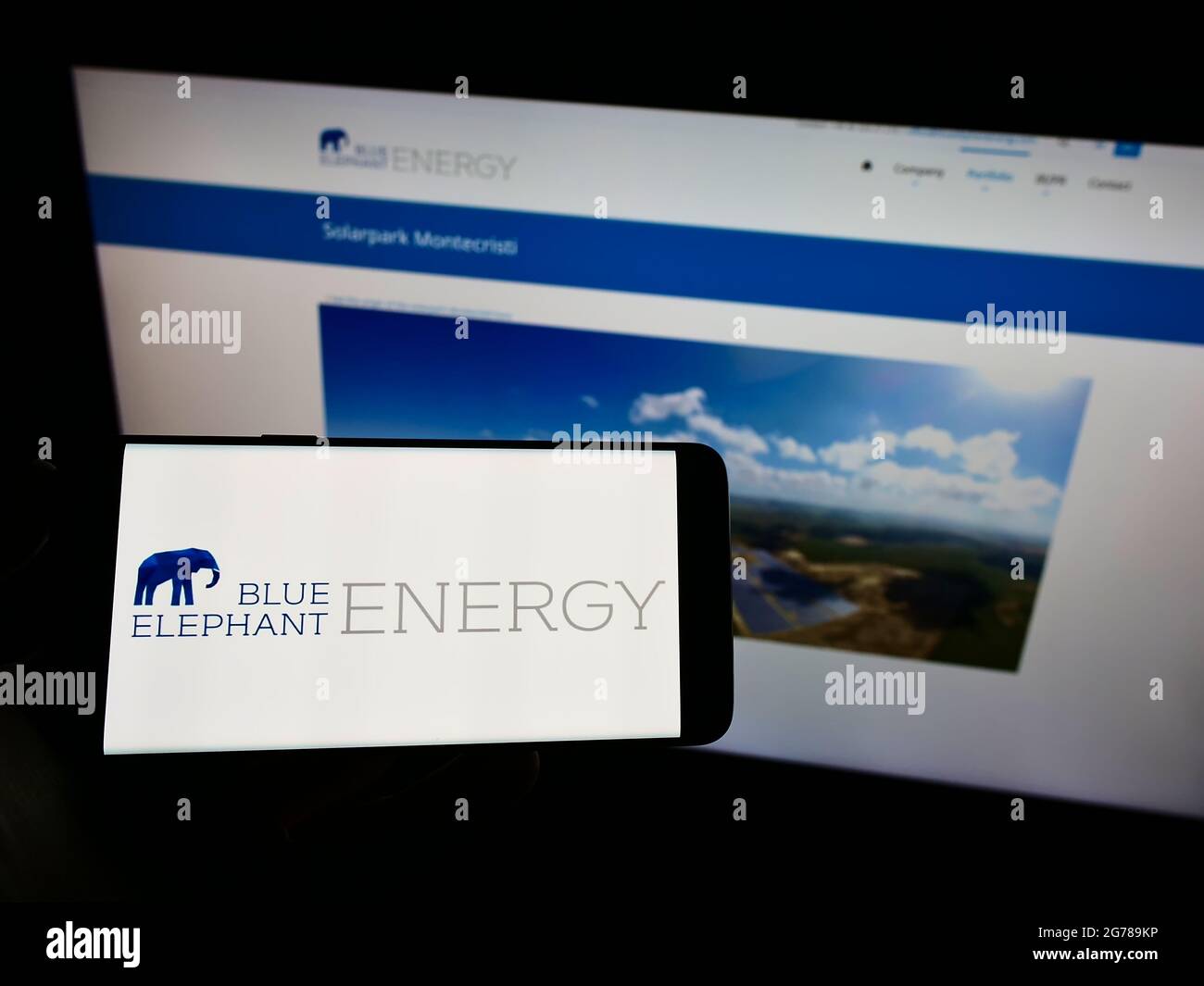 Persona che tiene il telefono cellulare con il logo della società tedesca di energia solare Blue Elephant Energy AG sullo schermo di fronte alla pagina web. Mettere a fuoco il display del telefono. Foto Stock