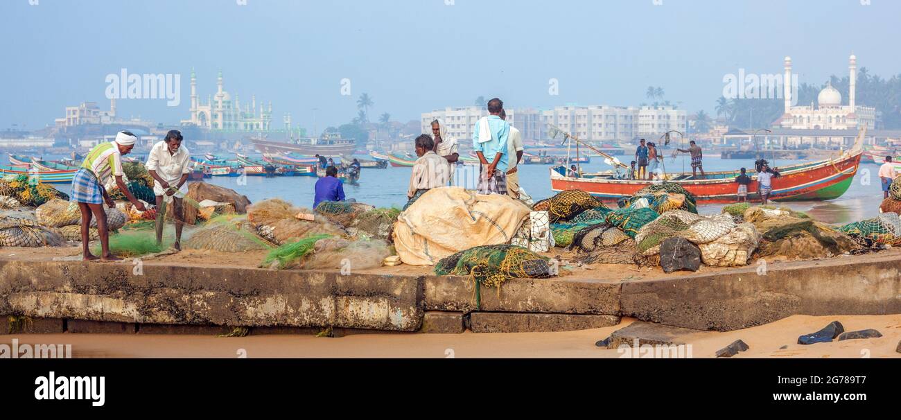 Panorama di pescatori indiani che tende la loro rete sul lungomare di Vizhinjam con moschee in background, Kerala, India Foto Stock