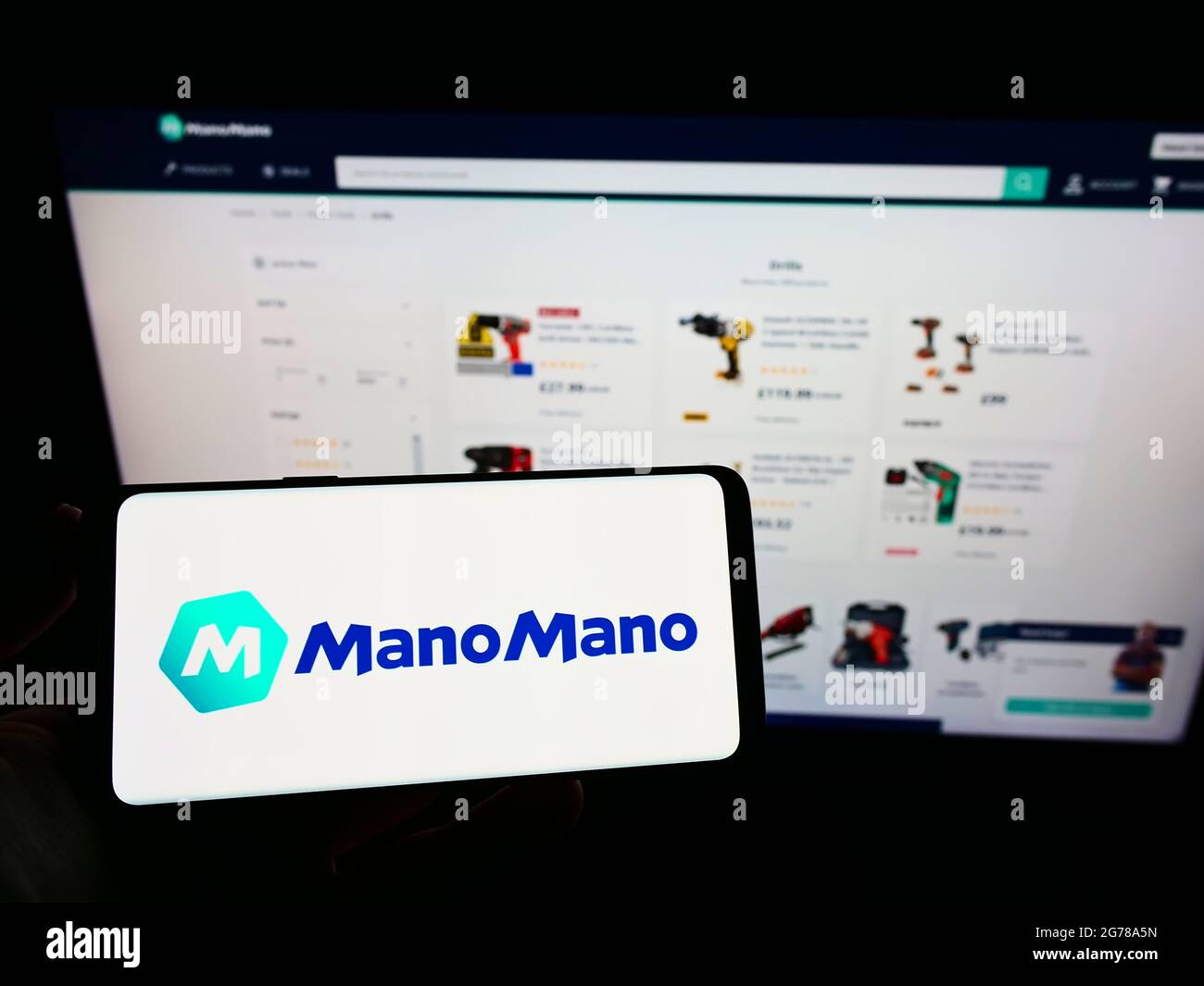 Persona che detiene il cellulare con il logo del mercato francese online ManoMano (Colibri SAS) sullo schermo davanti alla pagina web. Mettere a fuoco il display del telefono. Foto Stock