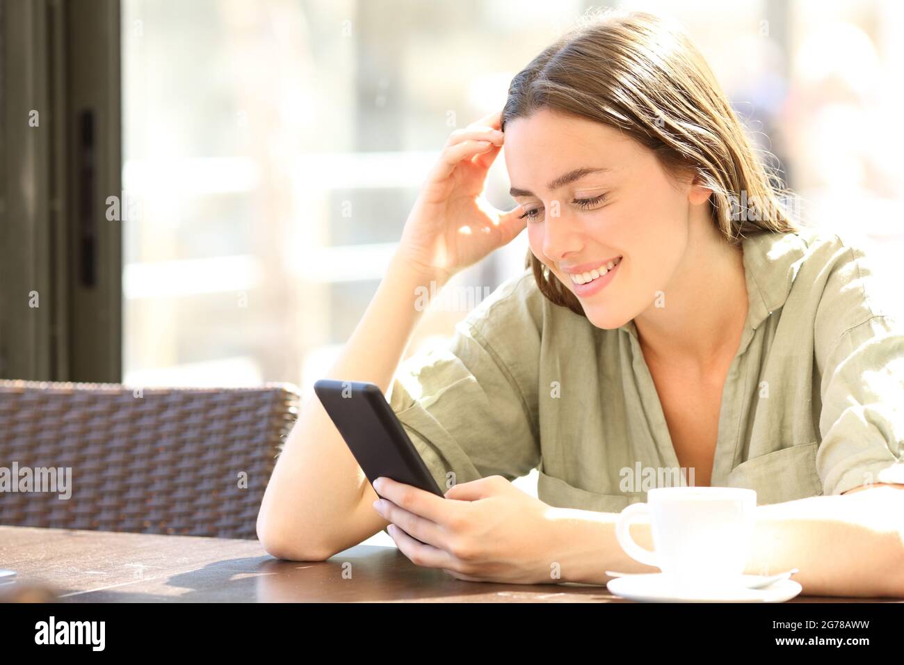 Donna felice sorridente che controlla il contenuto dello smartphone seduto in una caffetteria Foto Stock
