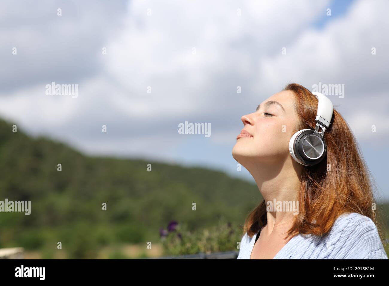 Donna rilassata che medita l'audio guida sulle cuffie respirando aria fresca in natura Foto Stock