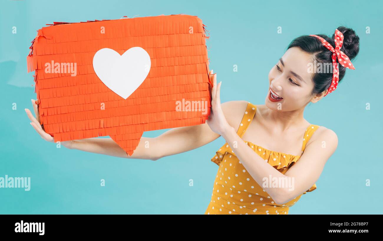 Attraente donna che tiene il simbolo del cuore di come e amore icona di notifica dei social media felice con i seguaci e i fan su Internet. Foto Stock