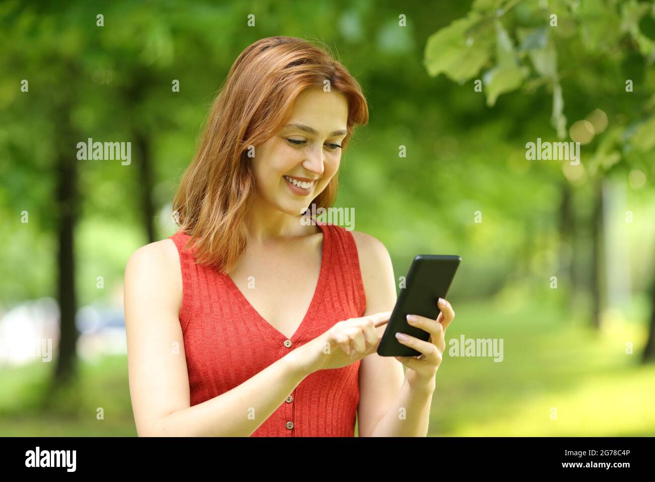 Donna felice in rosso con il telefono cellulare che cammina in un parco Foto Stock