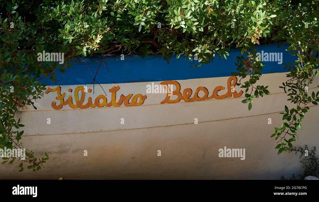 Isole IONIE, Ithaka, isola di Odysseus, vicino a Vathi, Filiatro Beach, Spiaggia di ghiaia, barca tirata a terra sotto i cespugli con l'iscrizione "Filiatro Beach" Foto Stock