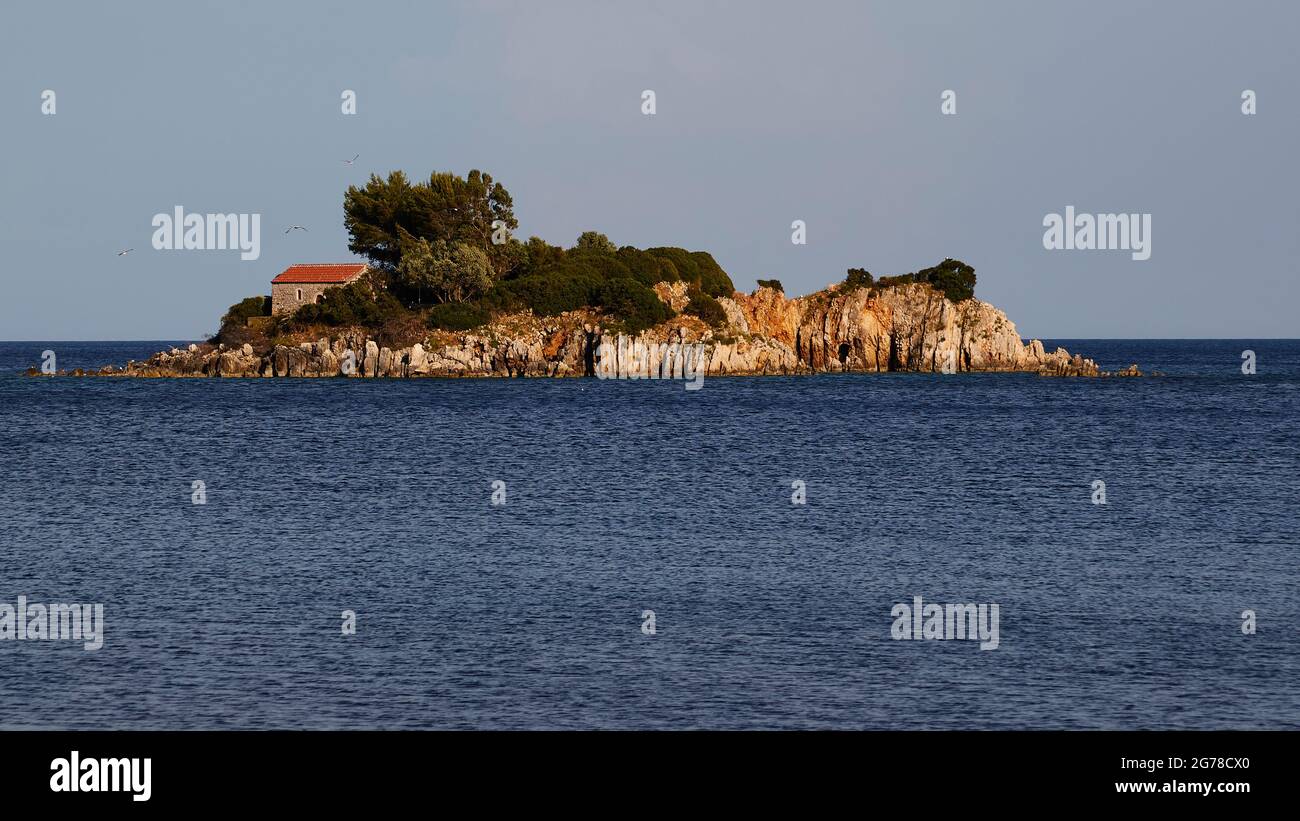 Isole IONIE, Ithaca, isola di Odysseus, costa nord-orientale, Baia di Marmakas, Isolotto di Agios Nikolaos dalla spiaggia, mare blu scuro, cielo azzurro chiaro, cappella con tetto rosso sul lato sinistro dell'isola, alberi e altre vegetazione accanto ad essa Foto Stock