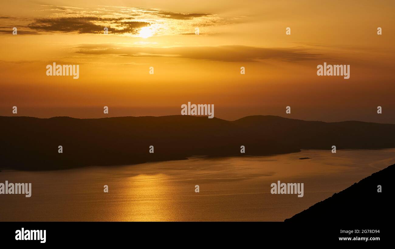 Isole IONIE, Ithaca, isola di Ulisse, tramonto su Kefaloniá, vista dalla costa occidentale di Ithaka attraverso lo stretto a Kefaloniá, tramonto dietro nuvole grigie in un cielo arancione, fascio di sole sul mare Foto Stock