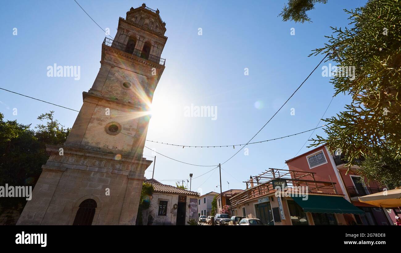 Isole IONIE, Zante, villaggio Kiliomenos, torre della chiesa, vista grandangolare da diagonalmente sotto destra, leggera distorsione, raggi solari dietro la torre della chiesa, luce posteriore, cielo blu Foto Stock