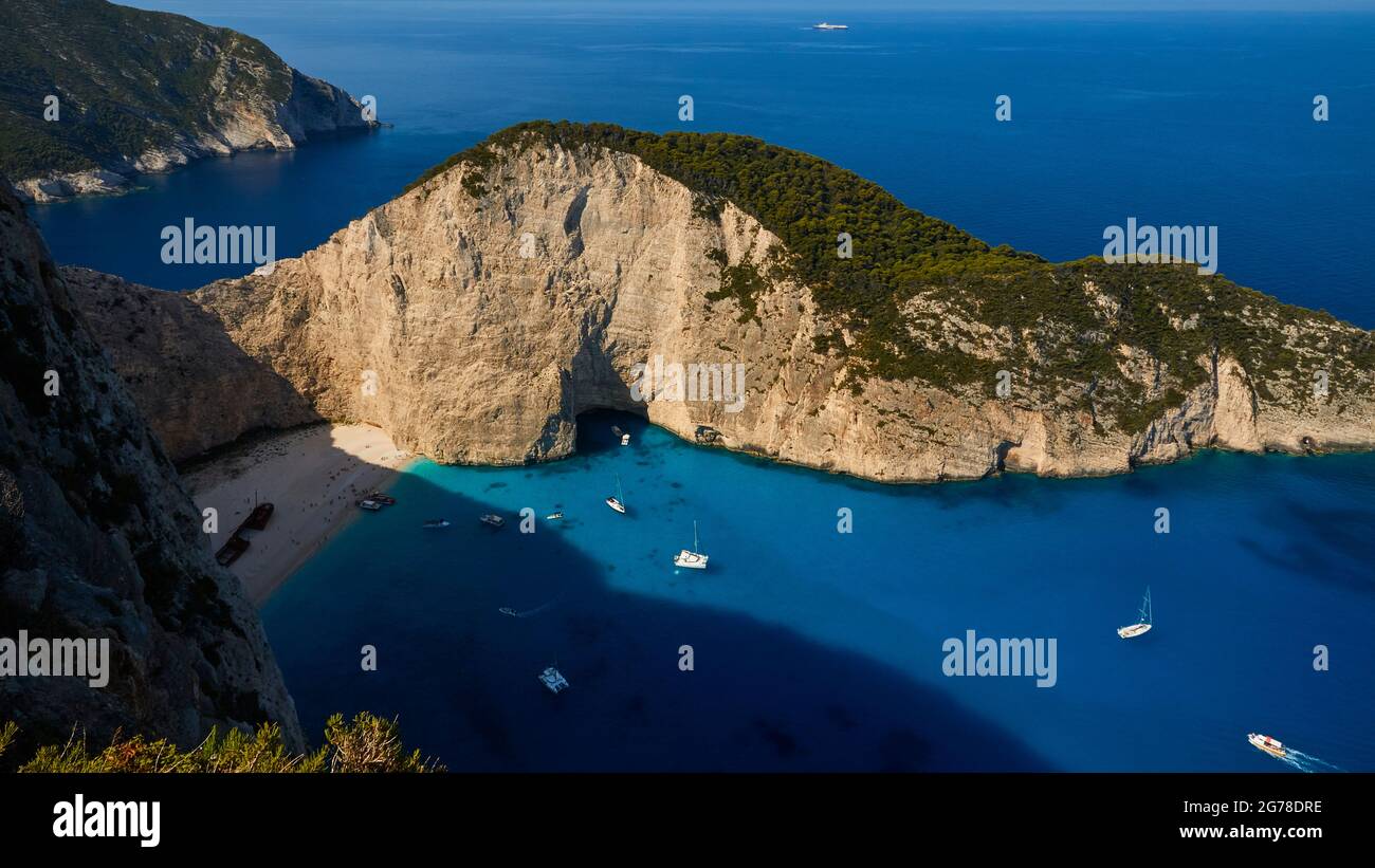 Zakynthos, Paralia Navagio, Shipwreck Beach, vista dall'alto verso e sopra la baia e la spiaggia parzialmente ombreggiata Navagio Beach, relitto MV Panagiotis all'ombra, escursioni barche all'ancora, barche a vela all'ancora, acque blu e turchesi, senza cielo Foto Stock