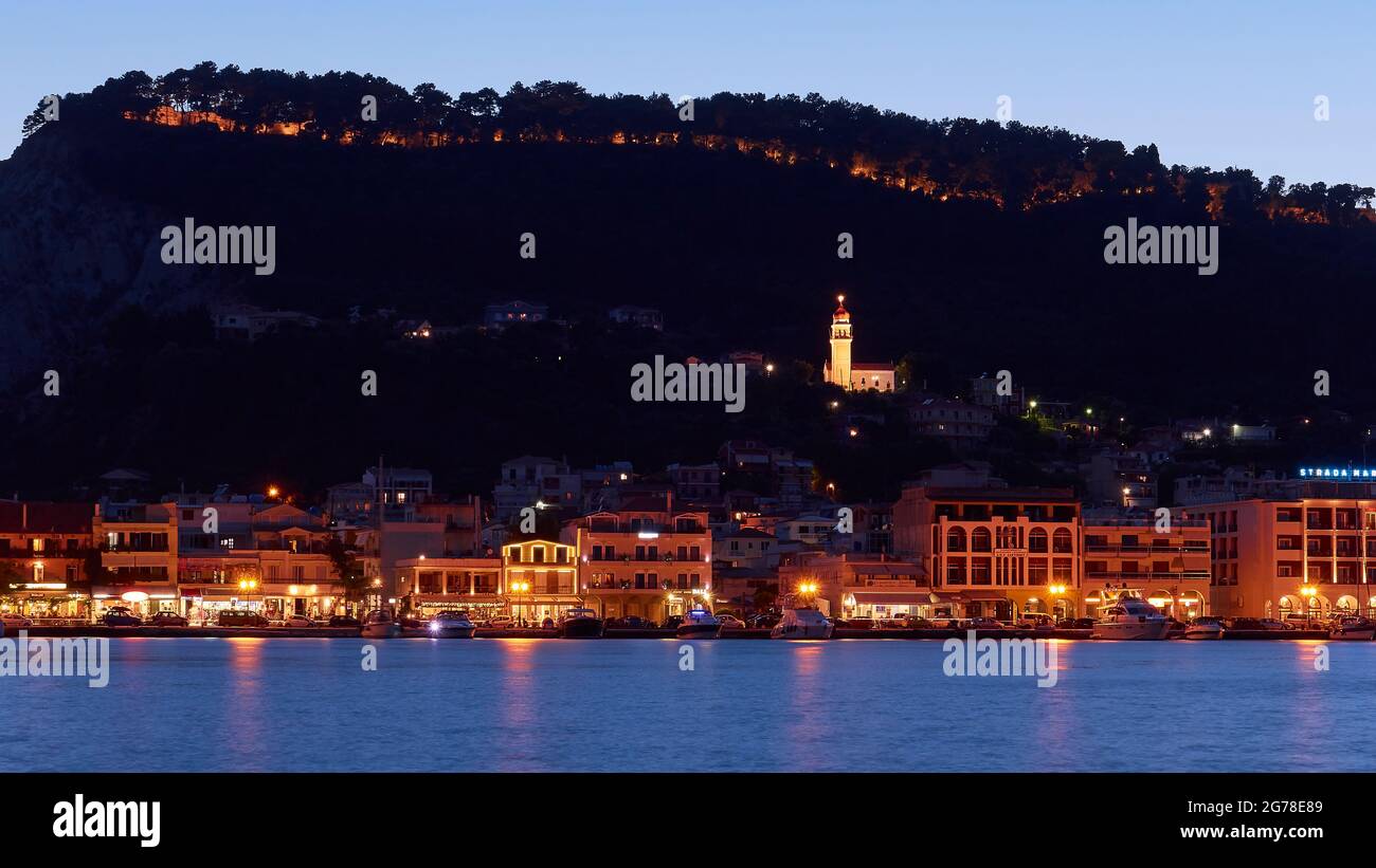 Zakynthos, Zakynthos City, foto notturna, foto serale, sezione dello skyline notturno di Zakynthos City, acqua in primo piano, edificio e Agias Triadas chiesa in mezzo, collina scura castello sullo sfondo, cielo blu sera Foto Stock