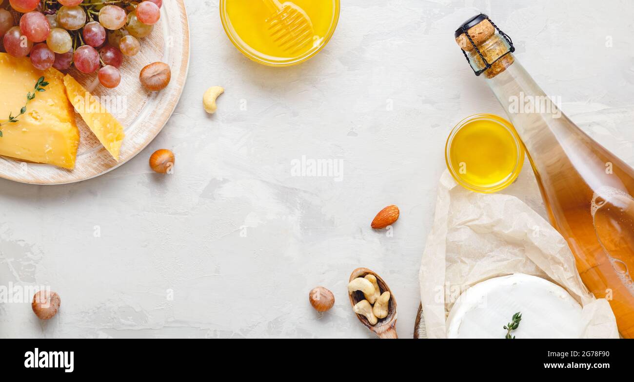Composizione del vino su fondo rustico in cemento grigio chiaro. Cornice in rosa bottiglia di vino formaggio noci e uva miele. Formaggio Camembert, vino Foto Stock