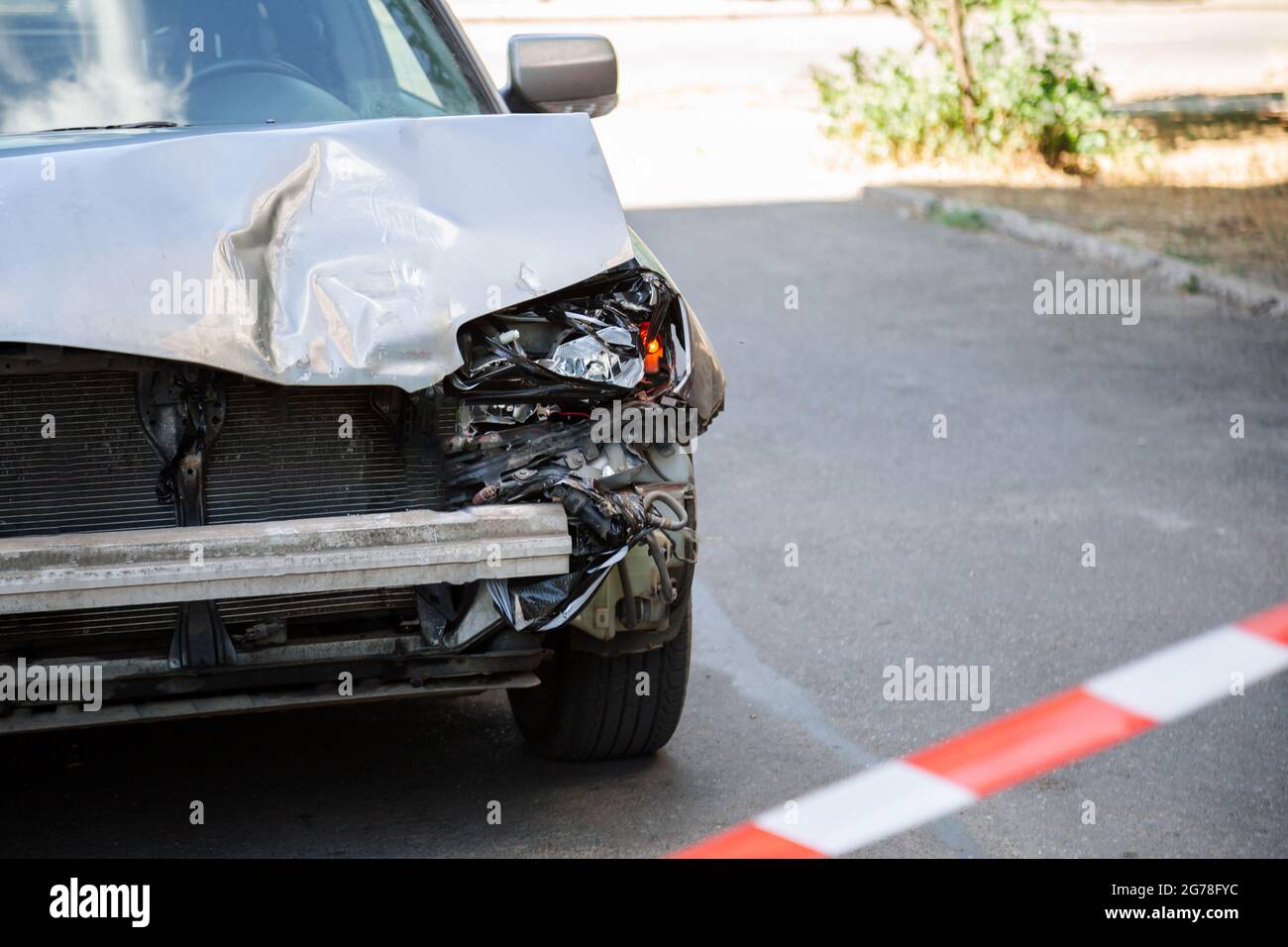 Incidente auto recintato con nastro di avvertimento rosso. Il cofano dell'auto su strada è rotto. Paraurti rotto e Fari auto con luce su asfalto stradale con copia Foto Stock