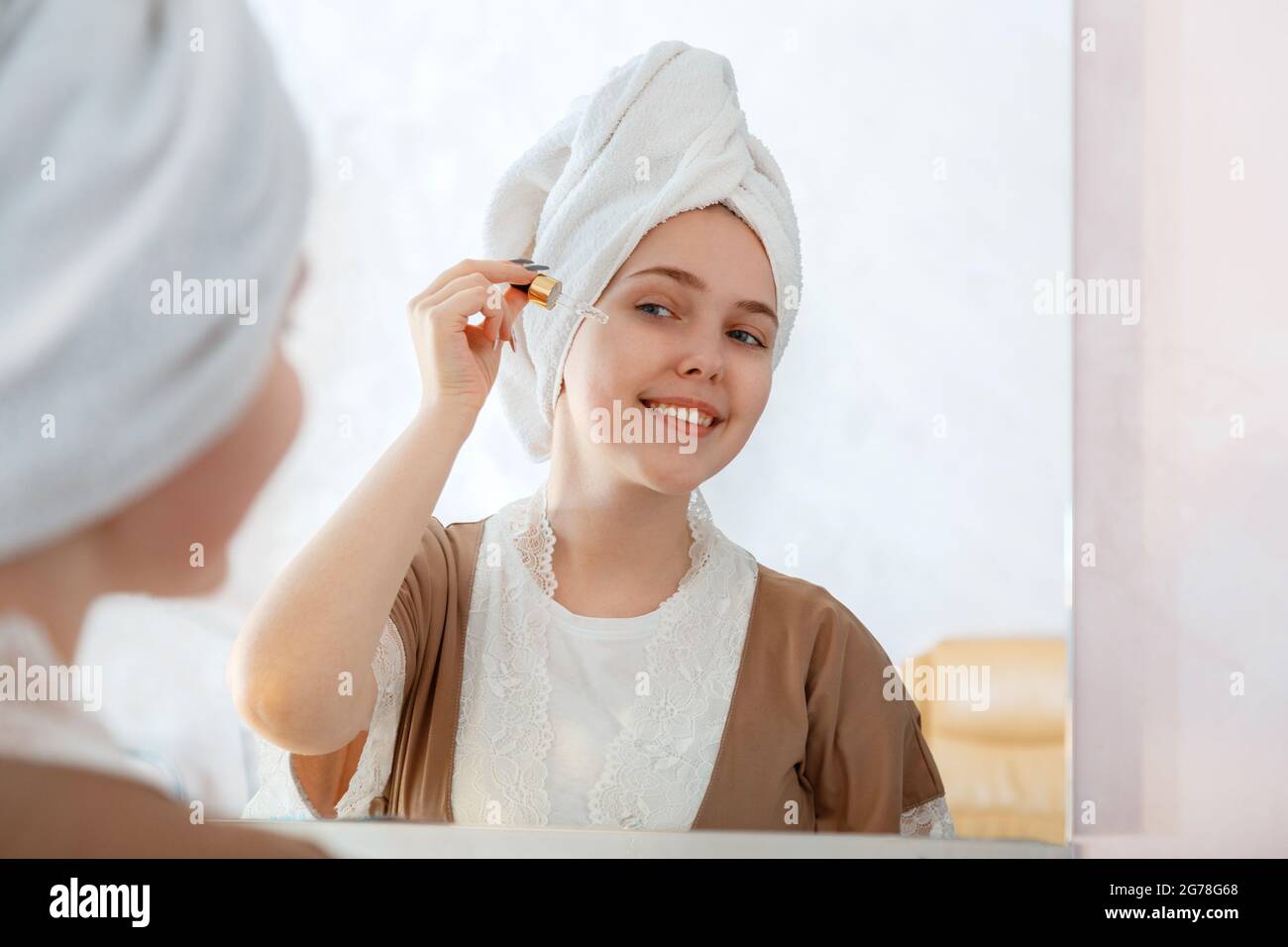 Giovane bella donna applica siero di olio in Dropper per la cura della pelle in bagno vicino a specchio. Prodotto cosmetico self-care nella routine mattutina. Giovane grazioso Foto Stock