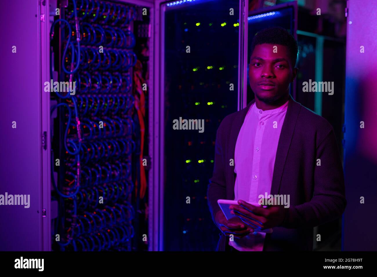 Ritratto di un giovane ingegnere afro-americano del data center che utilizza un tablet digitale durante il controllo della connessione al server Foto Stock