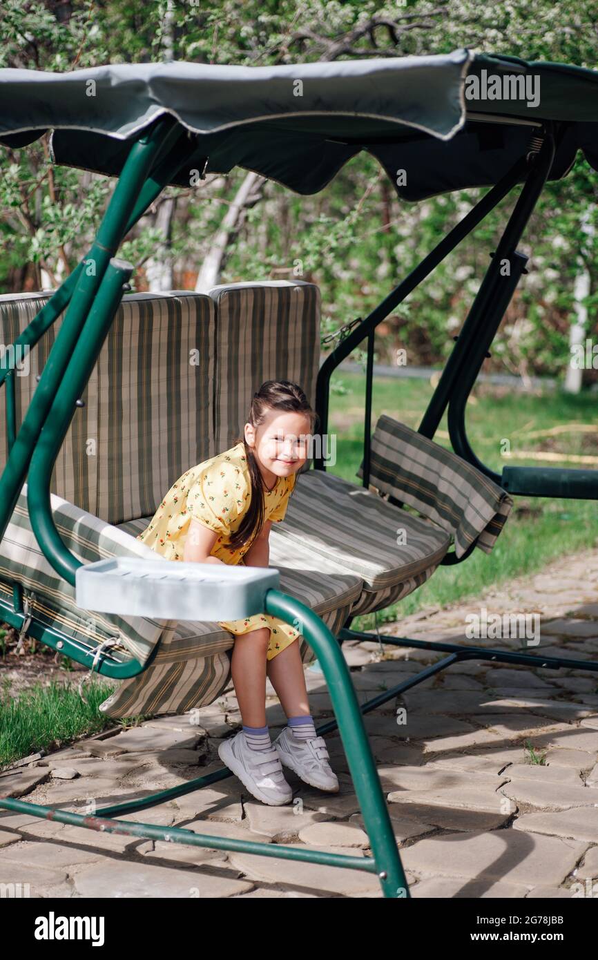 un bambino felice e sorridente corre su un'altalena nel cortile, il bambino ha divertimento sull'altalena in estate Foto Stock