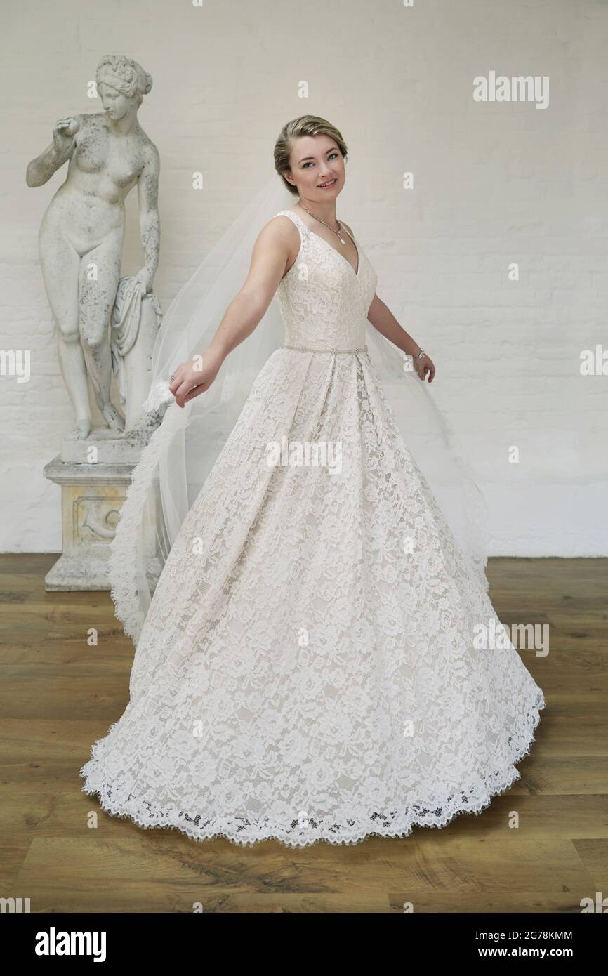 Sposa in un abito da sposa in avorio con un velo orlato in pizzo e un grande bouquet floreale color pastello. Foto Stock