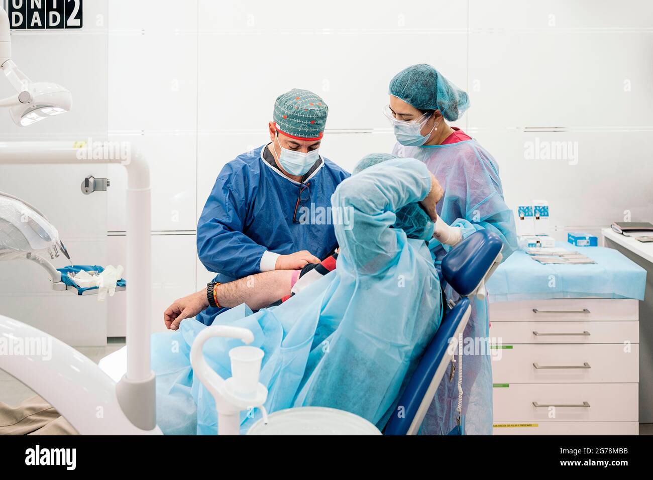 Smiley medico che lavora in clinica che preleva sangue a pazienti senza volto. Indossa una maschera facciale e indumenti protettivi. Foto Stock