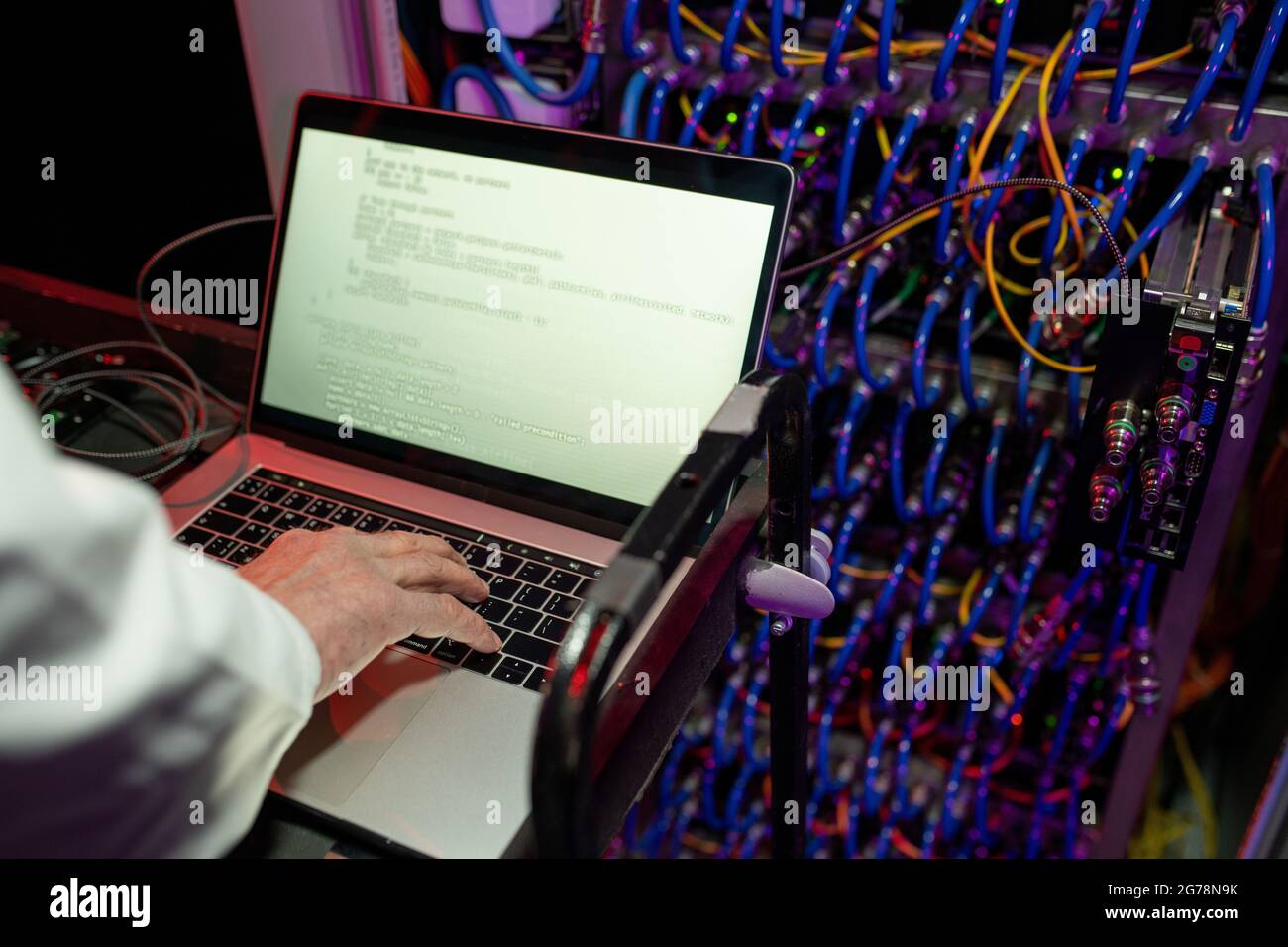 Primo piano di un tecnico irriconoscibile che si trova al carrello contro l'armadietto del server e che imposta il server utilizzando un laptop Foto Stock