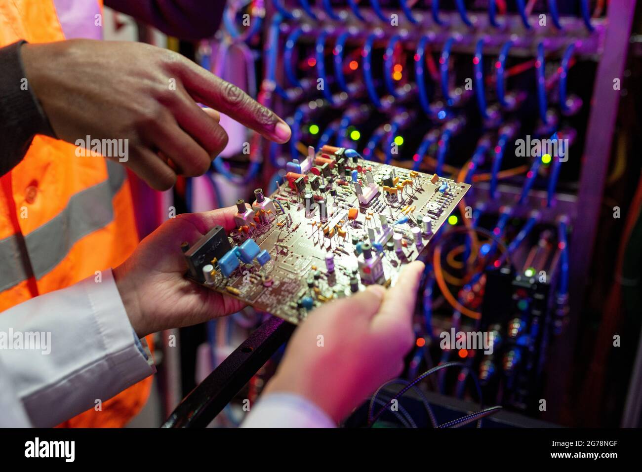 Primo piano di un ingegnere nero che punta alla scheda a circuiti stampati del computer mentre ne discute la struttura con un collega Foto Stock