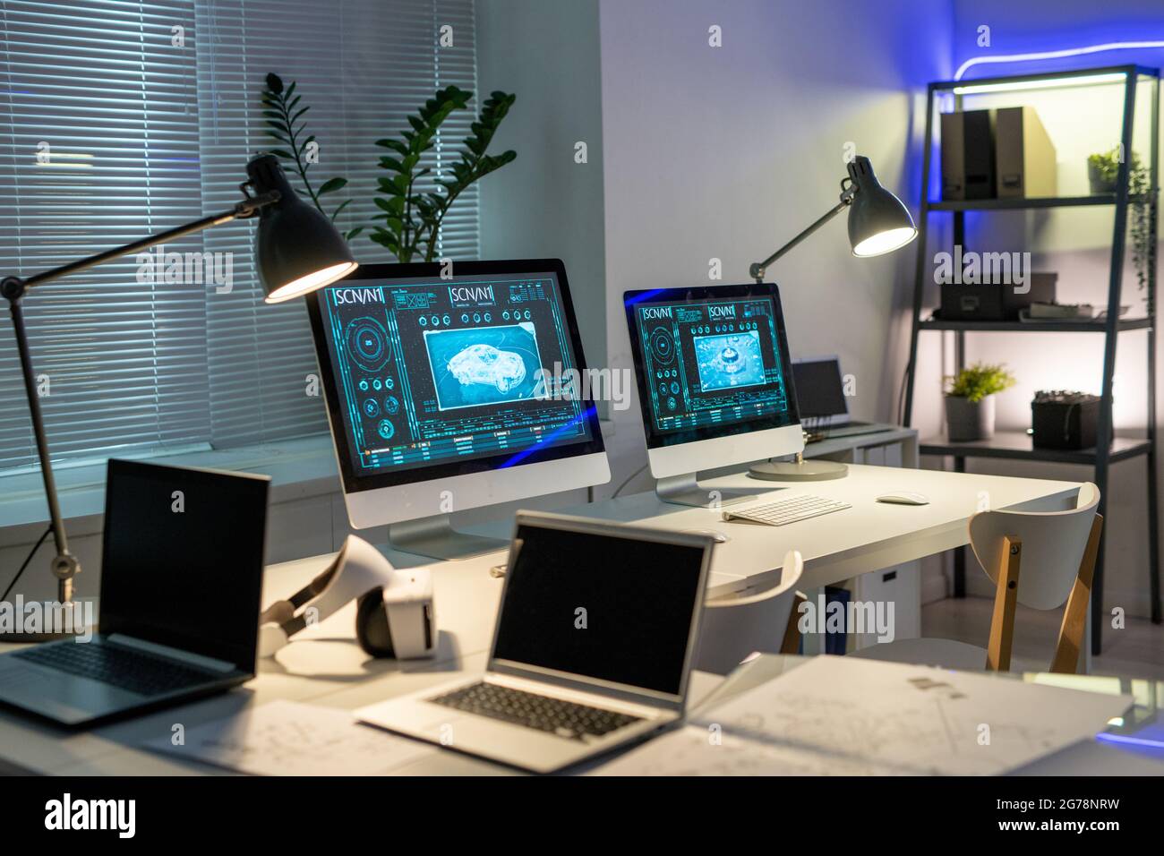 Vuoto ufficio contemporaneo di azienda di disegno di automobile con le immagini di automobile sui monitor del calcolatore sui tavoli illuminati con le lampade Foto Stock