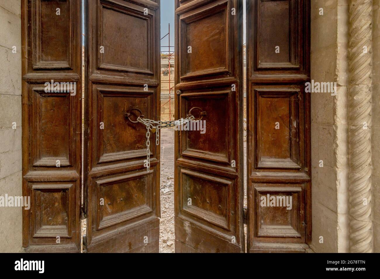 Una porta di legno chiusa da una catena con lucchetto all'ingresso di uno dei tanti edifici distrutti dal terremoto del 2016, Norcia, Italia Foto Stock