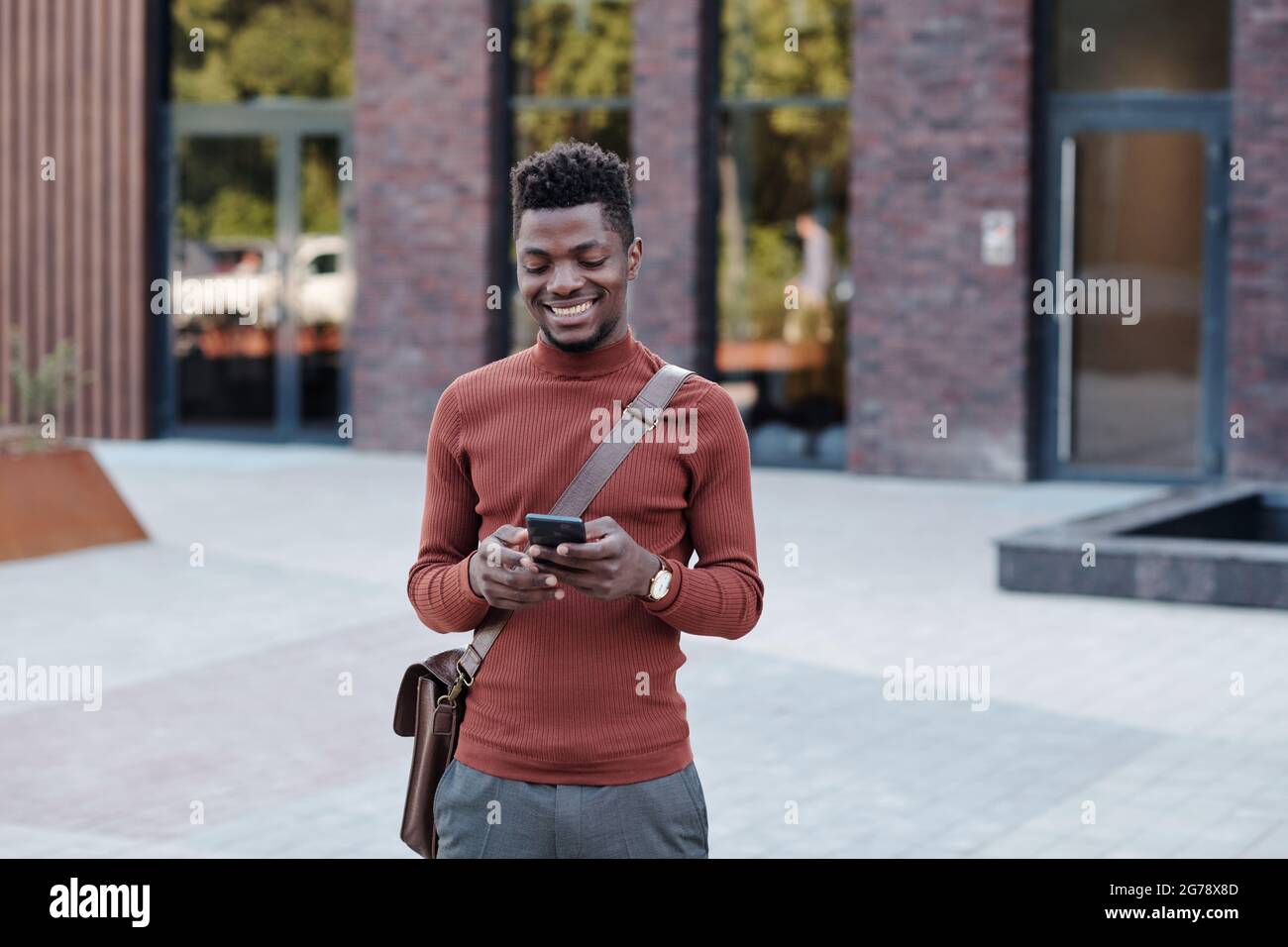 Felice giovane uomo d'affari di etnia africana utilizzando smartphone in strada Foto Stock