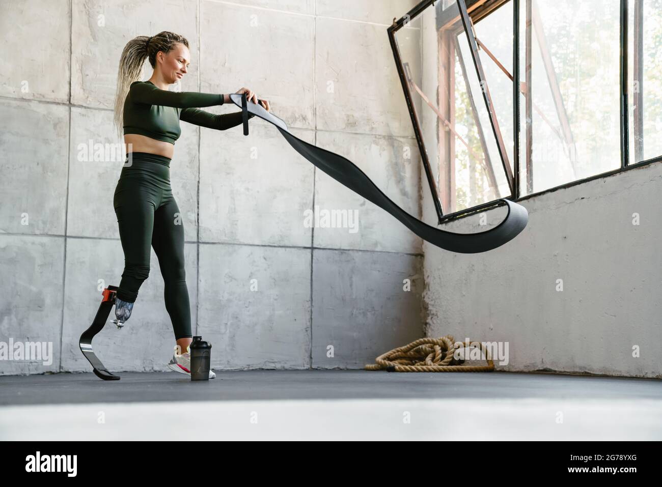 Giovane sportivo con protesi srotolante materassino fitness interno Foto Stock